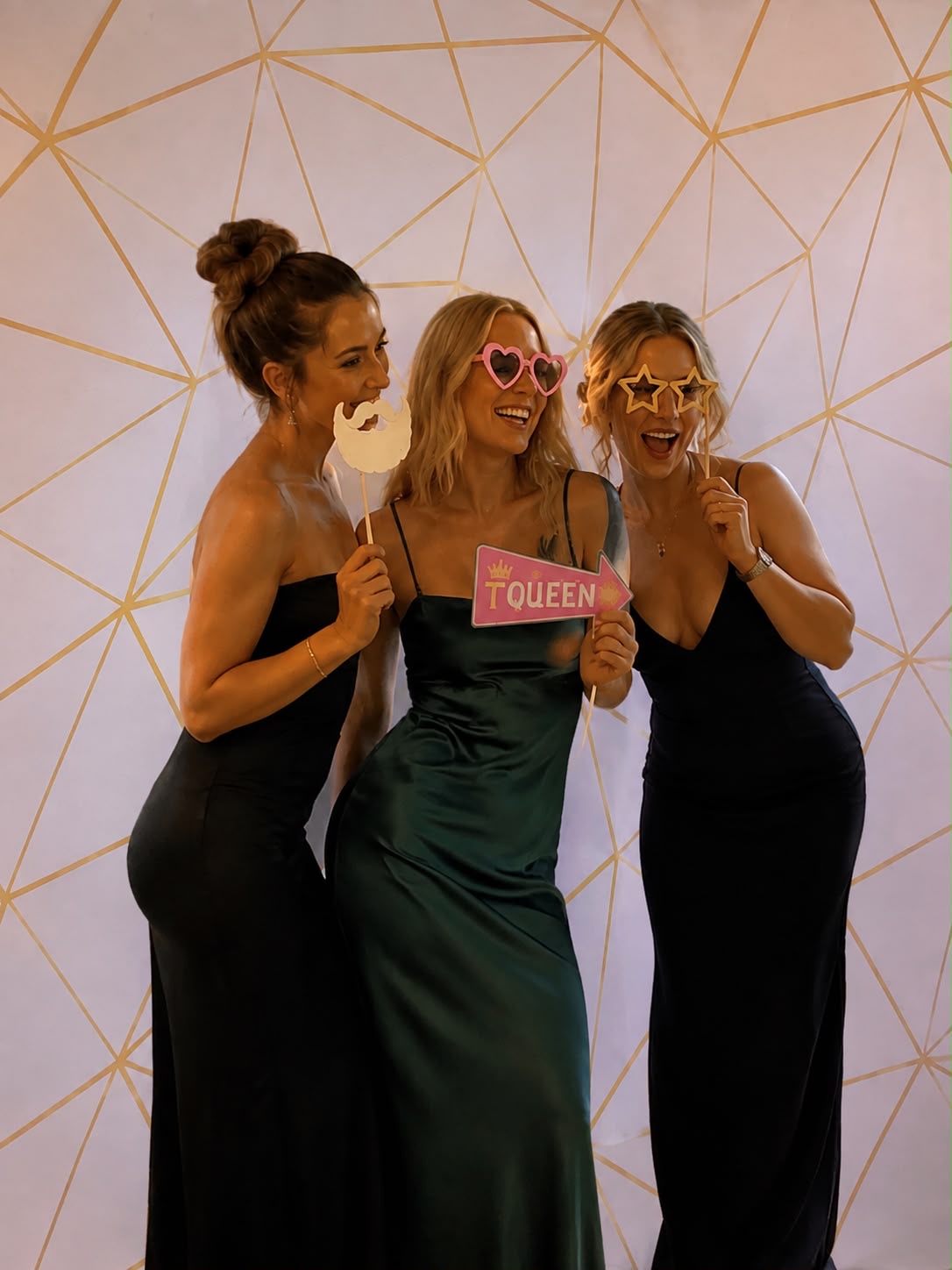 Three guests posing with fun props in front of a white and gold geometric backdrop